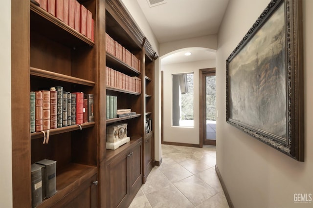 hallway with arched walkways, baseboards, and light tile patterned floors