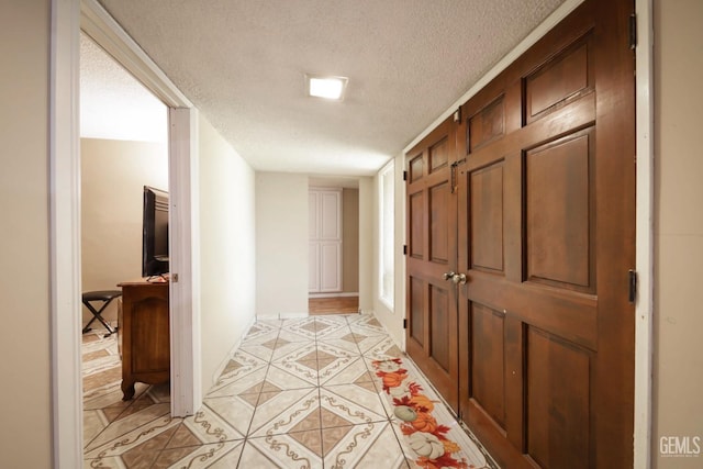 hall with a textured ceiling and light tile patterned flooring