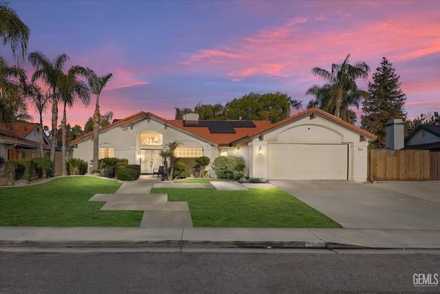 mediterranean / spanish house with a garage, solar panels, fence, a yard, and driveway