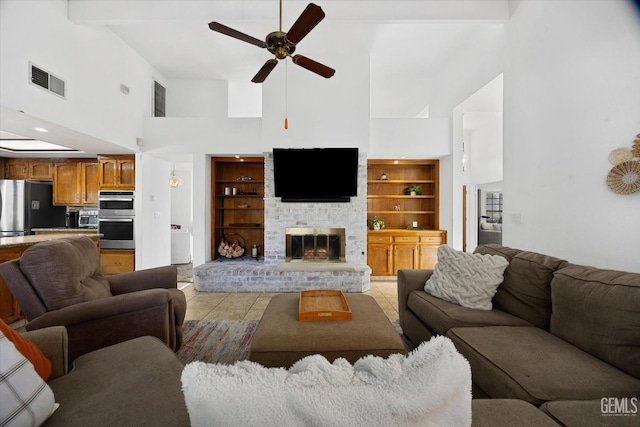 living area with built in shelves, light tile patterned floors, visible vents, a ceiling fan, and a large fireplace