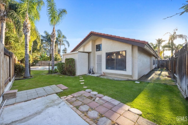 rear view of house with a fenced backyard, a tile roof, a yard, stucco siding, and a patio area