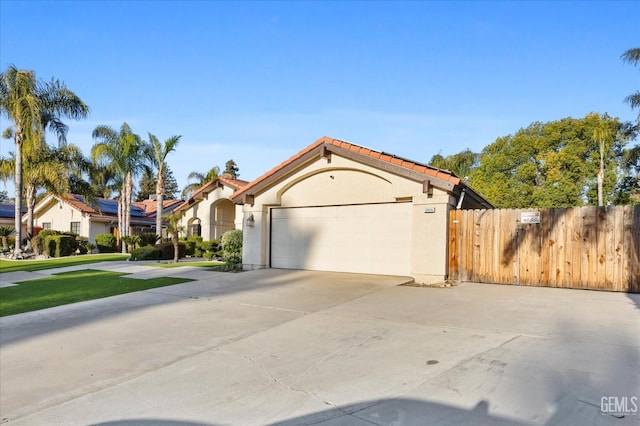 mediterranean / spanish house with an attached garage, fence, a tile roof, concrete driveway, and stucco siding