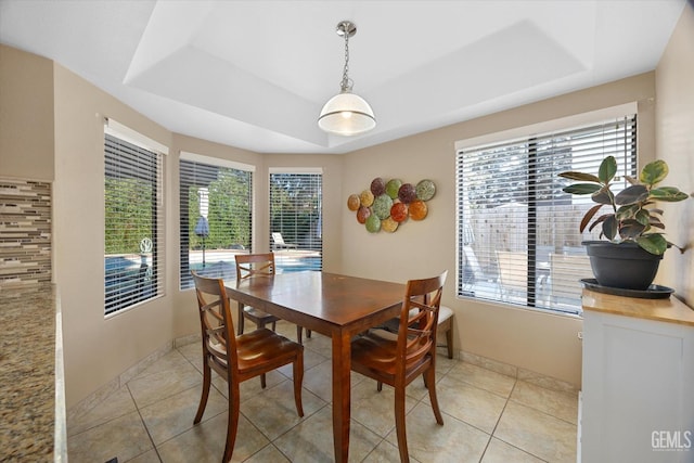 dining area featuring a raised ceiling, baseboards, and light tile patterned floors