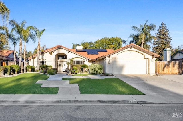 mediterranean / spanish-style house with solar panels, an attached garage, fence, driveway, and a front lawn