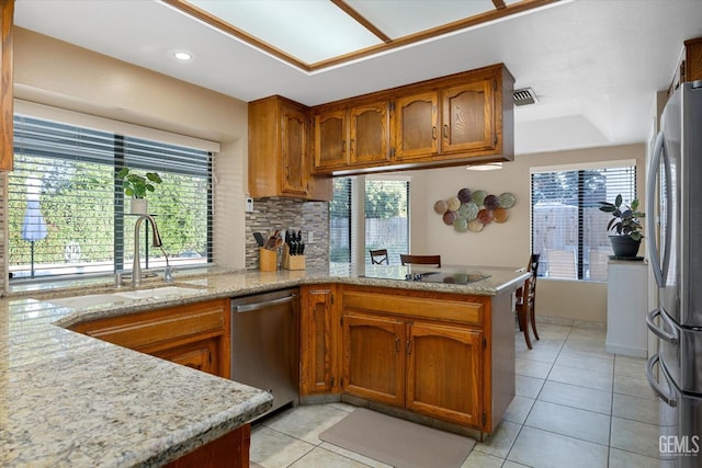 kitchen featuring stainless steel appliances, a peninsula, visible vents, brown cabinets, and tasteful backsplash