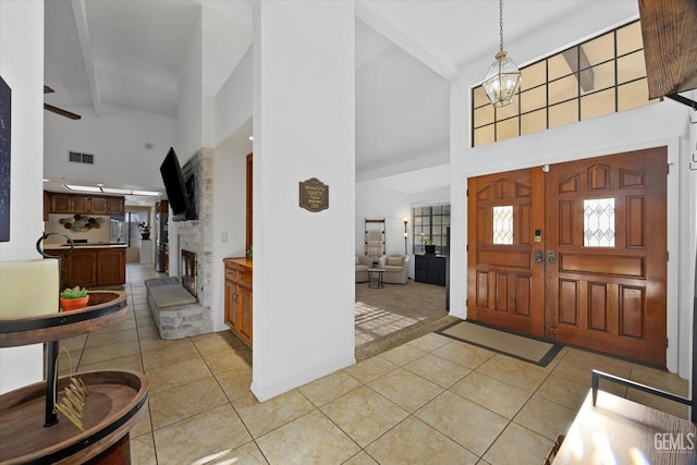 foyer entrance featuring beam ceiling, visible vents, light tile patterned flooring, a stone fireplace, and a chandelier