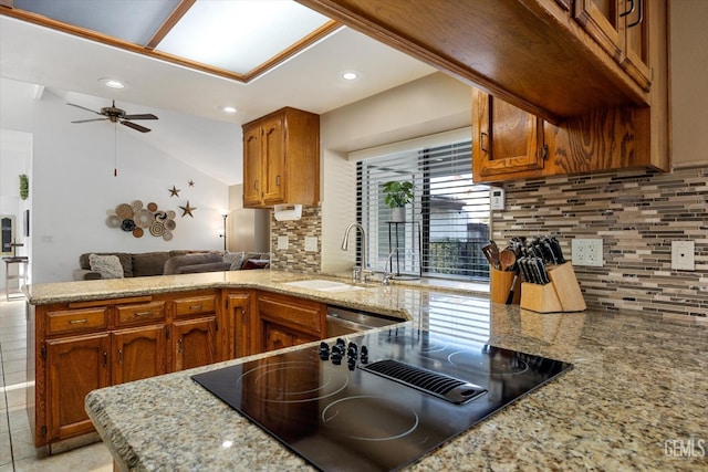 kitchen featuring black electric stovetop, brown cabinetry, open floor plan, a sink, and a peninsula