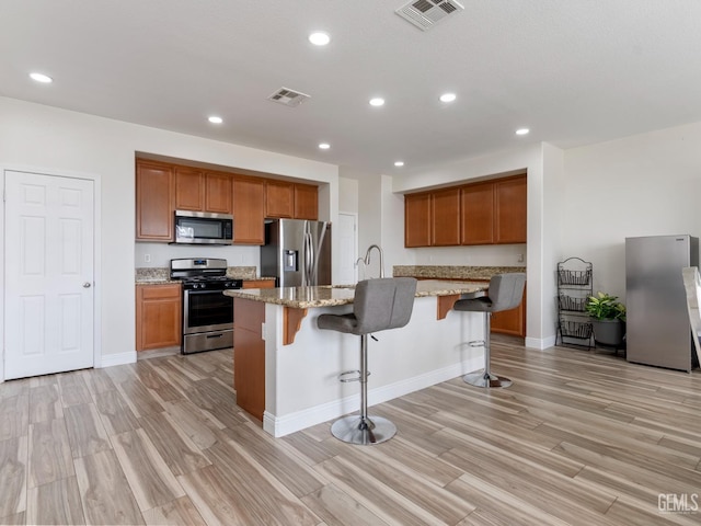 kitchen featuring visible vents, an island with sink, a breakfast bar area, light stone countertops, and stainless steel appliances