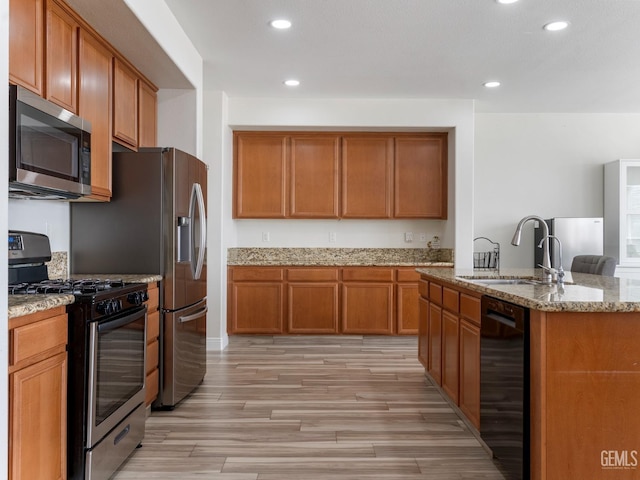 kitchen featuring brown cabinets, appliances with stainless steel finishes, light stone counters, and a sink