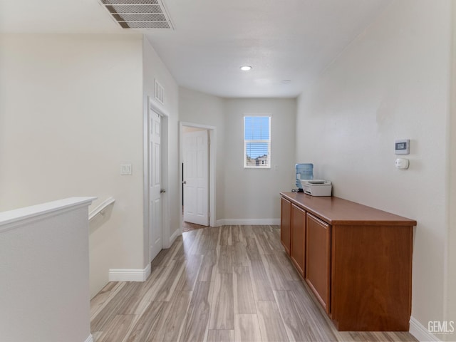 hall featuring light wood-style flooring, visible vents, baseboards, and an upstairs landing