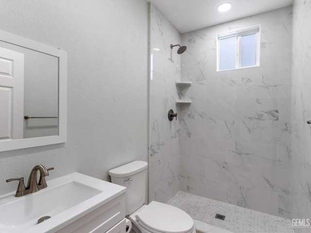 bathroom with toilet, a textured wall, a shower stall, and vanity