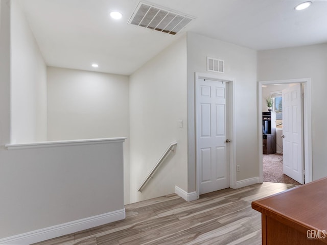 hallway with light wood-style flooring, an upstairs landing, visible vents, and recessed lighting