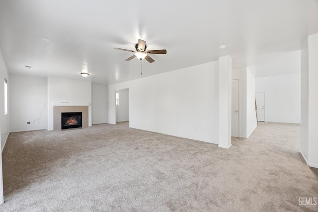 unfurnished living room featuring a tiled fireplace, light carpet, and ceiling fan