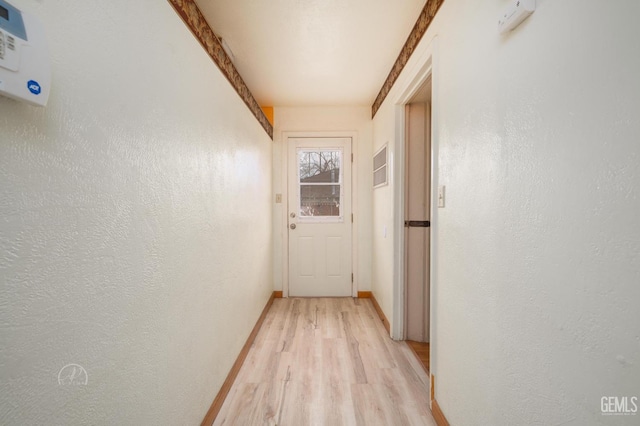 corridor with light wood-type flooring, baseboards, and a textured wall