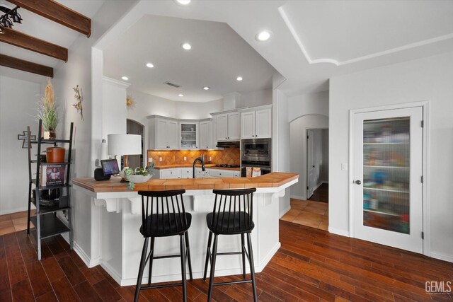 kitchen featuring decorative backsplash, a peninsula, butcher block counters, black oven, and glass insert cabinets