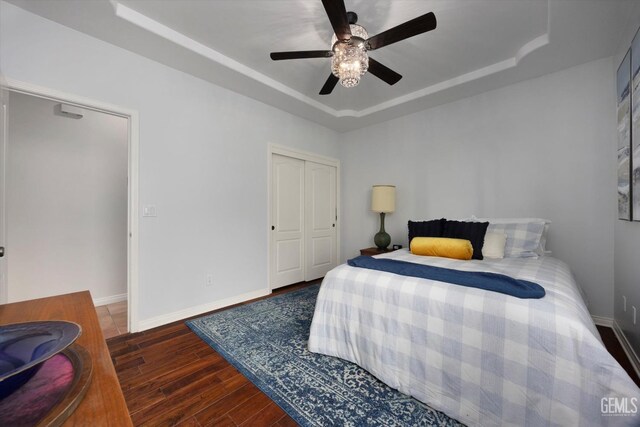 bedroom featuring a closet, baseboards, a raised ceiling, and wood finished floors