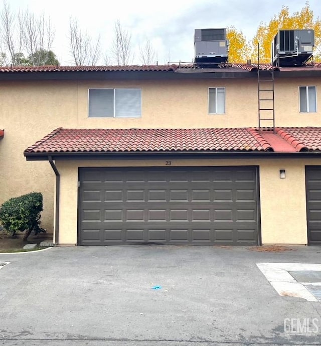 view of front facade with stucco siding, a tiled roof, an attached garage, and central AC unit