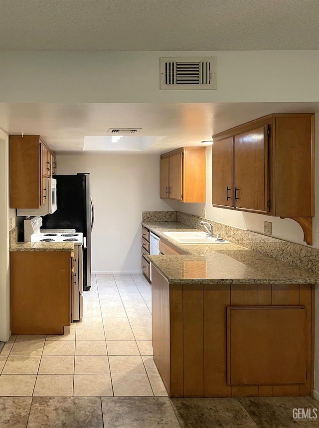 kitchen featuring visible vents, brown cabinetry, a sink, white appliances, and a peninsula