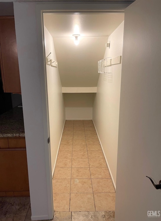 hall featuring light tile patterned flooring, vaulted ceiling, and baseboards