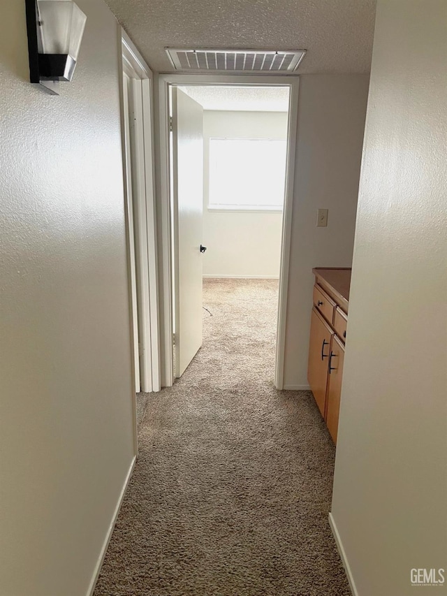 corridor with light carpet, a textured ceiling, visible vents, and baseboards