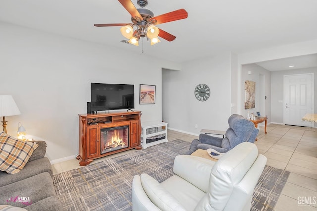 living area featuring a glass covered fireplace, light tile patterned flooring, baseboards, and ceiling fan