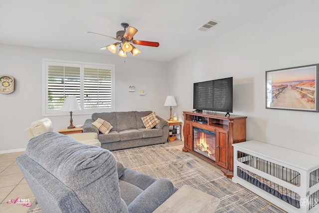 living room featuring visible vents, baseboards, light tile patterned flooring, a glass covered fireplace, and a ceiling fan