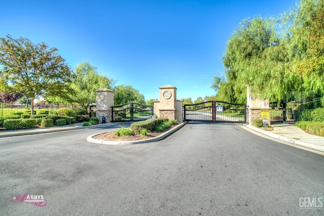 view of street with a gated entry, sidewalks, curbs, and a gate