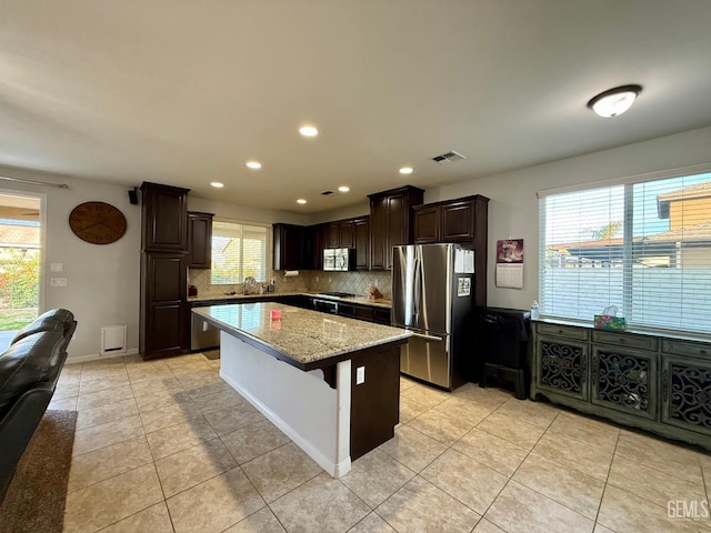 kitchen with decorative backsplash, light tile patterned floors, stainless steel appliances, and a kitchen island