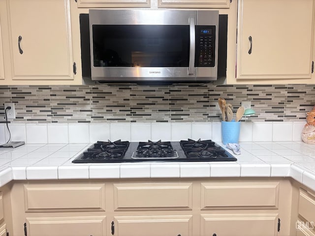 kitchen with cream cabinetry, stainless steel microwave, and tile countertops