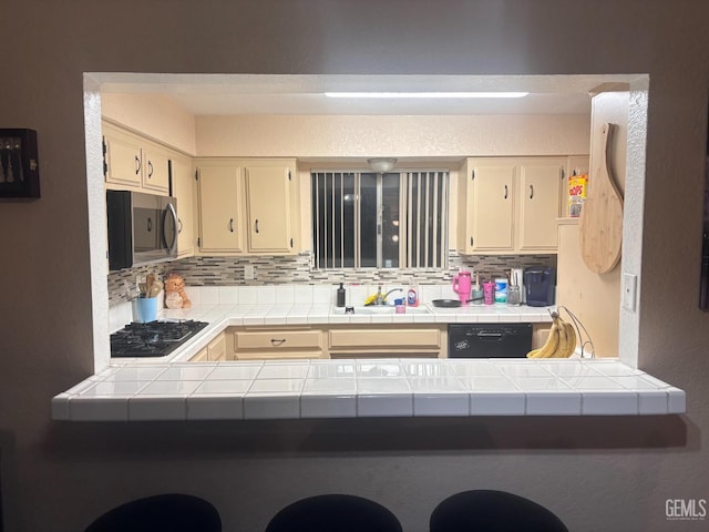 kitchen featuring tile countertops, a sink, black dishwasher, tasteful backsplash, and stainless steel microwave