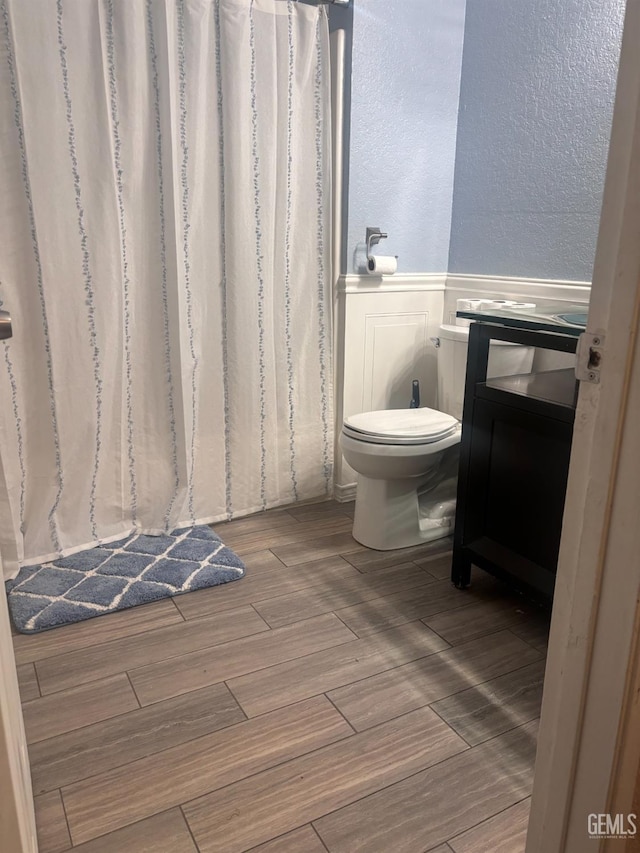 bathroom with a textured wall, wood finish floors, vanity, and toilet