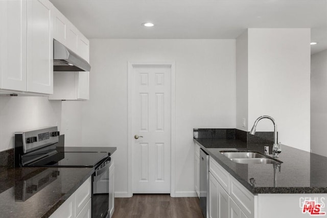 kitchen with sink, white cabinetry, dark stone counters, stainless steel appliances, and wall chimney range hood