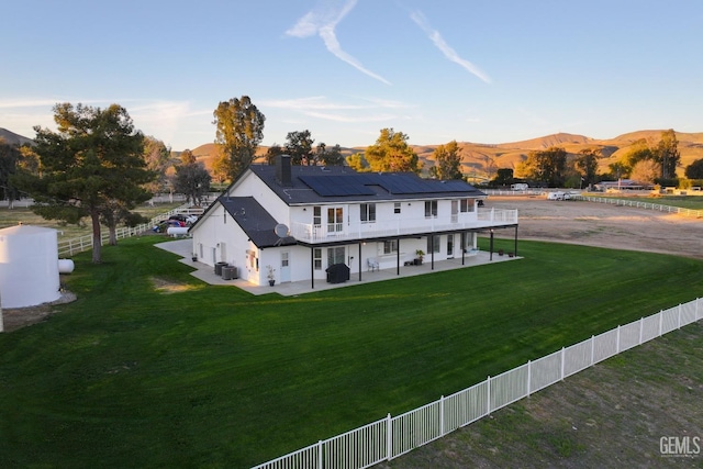 view of front of house with roof mounted solar panels, a fenced backyard, a mountain view, a front yard, and a patio area