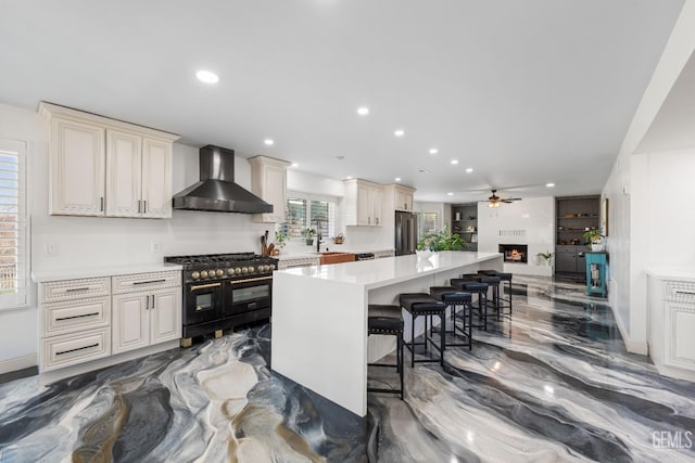 kitchen with marble finish floor, double oven range, freestanding refrigerator, a breakfast bar area, and wall chimney exhaust hood