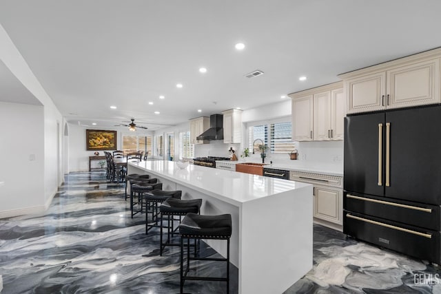 kitchen with wall chimney range hood, a breakfast bar, cream cabinets, marble finish floor, and black appliances