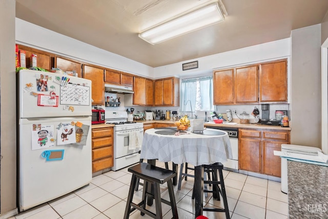 131 Eye St, Bakersfield, CA 93304 - kitchen with brown cabinets, under cabinet range hood, light tile patterned floors, and white appliances