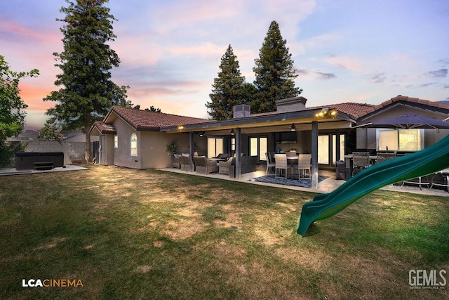 10005 Valley Forest Ct, Bakersfield, CA 93311 - back of house at dusk featuring a hot tub, a playground, a tiled roof, and a yard