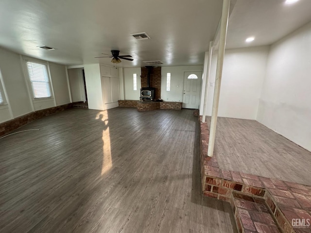 unfurnished living room featuring dark hardwood / wood-style floors, ceiling fan, and a wood stove