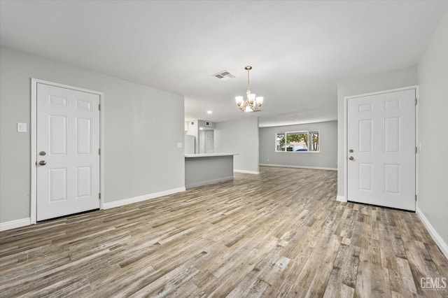 unfurnished living room featuring visible vents, baseboards, a chandelier, and wood finished floors