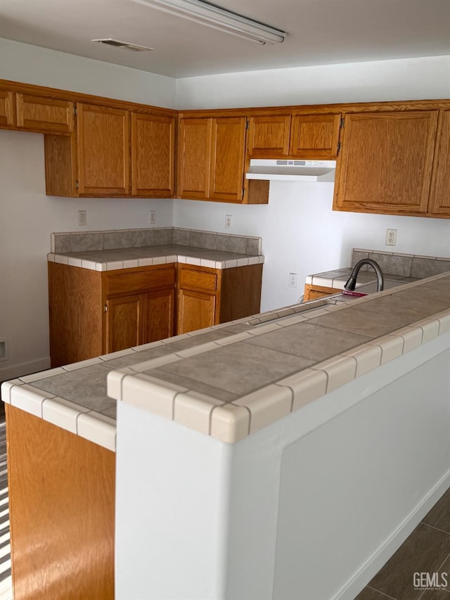kitchen with under cabinet range hood, visible vents, and brown cabinets