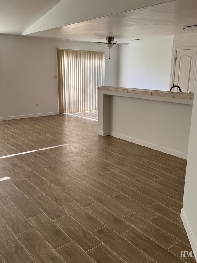unfurnished living room featuring dark wood-type flooring, baseboards, and ceiling fan