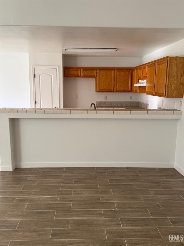 kitchen featuring brown cabinetry, tile counters, and dark wood-style floors
