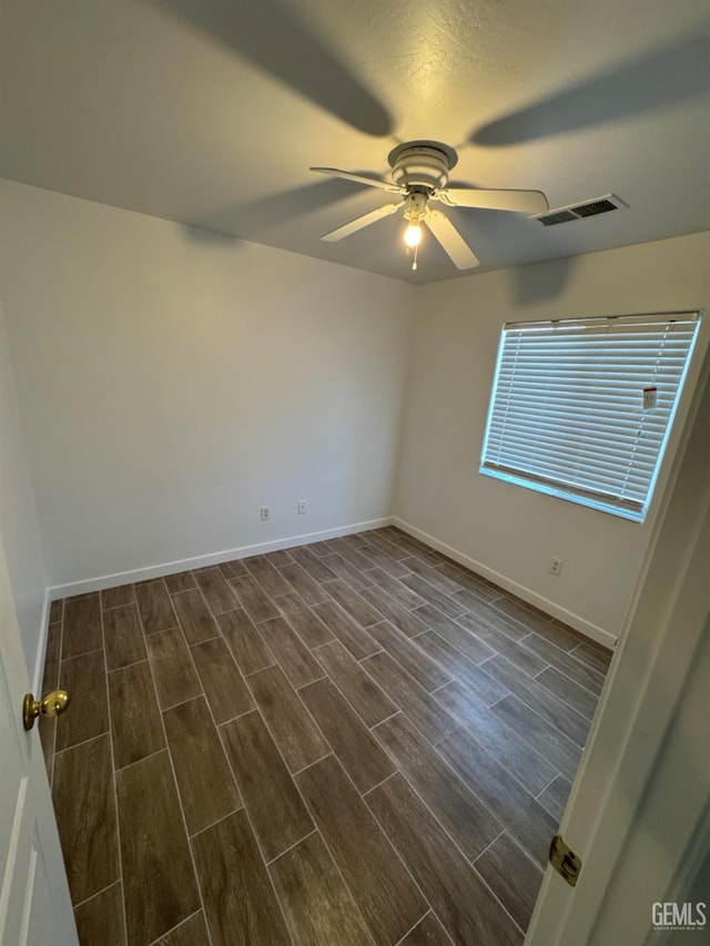 spare room featuring visible vents, ceiling fan, baseboards, and dark wood finished floors