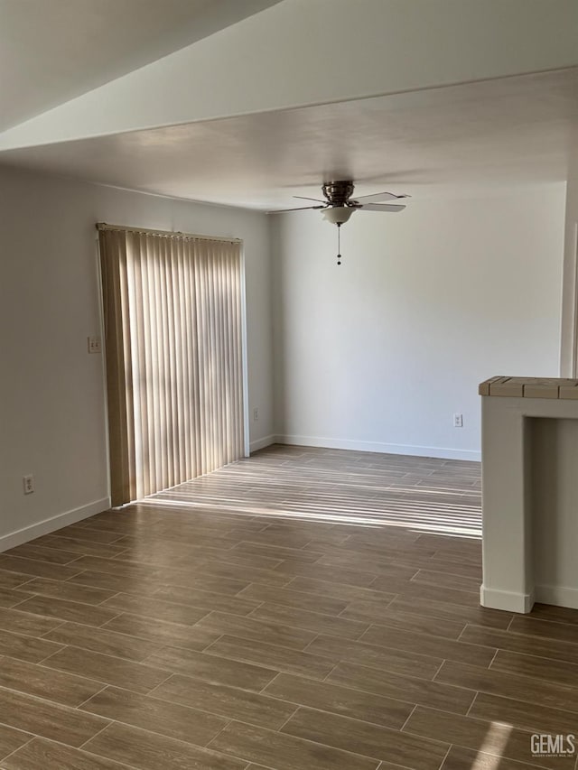 unfurnished room featuring dark wood-type flooring, ceiling fan, and baseboards