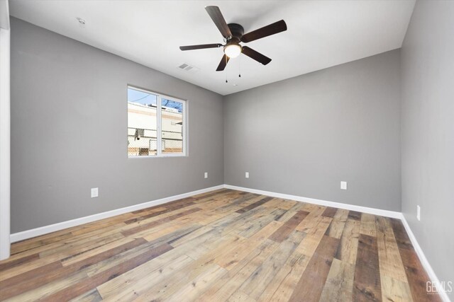 spare room featuring hardwood / wood-style flooring, baseboards, visible vents, and a ceiling fan