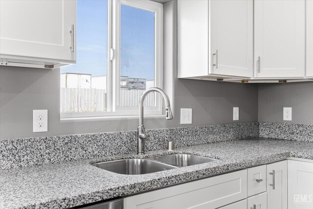 kitchen featuring a sink, light stone countertops, and white cabinets