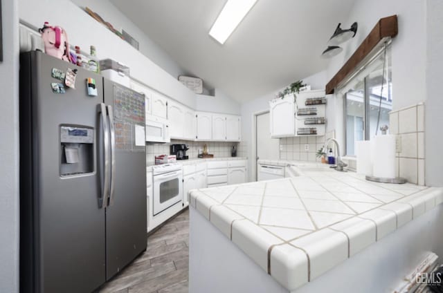 kitchen featuring a sink, tasteful backsplash, vaulted ceiling, tile countertops, and white appliances