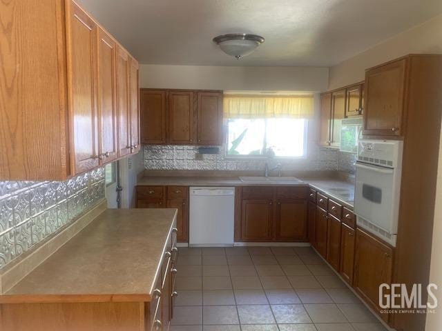 kitchen featuring tasteful backsplash, light tile patterned floors, a sink, white appliances, and brown cabinets