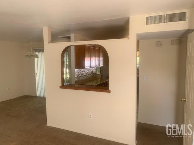 spare room with arched walkways, visible vents, and dark carpet