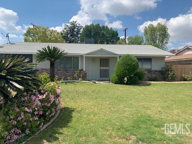 single story home with stone siding, fence, and a front lawn